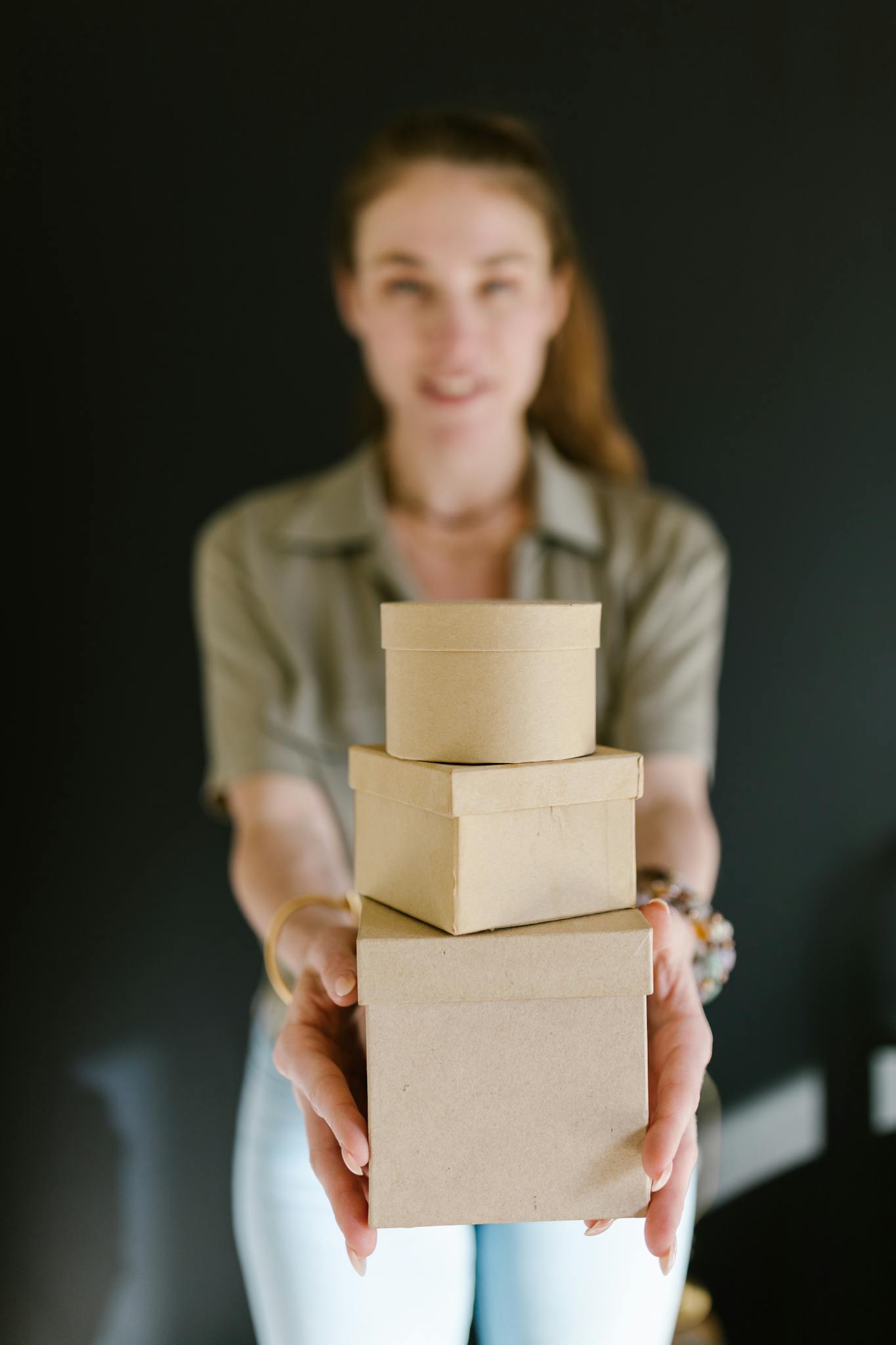 Our Mission Blurred woman holding a stack of cardboard boxes, ideal for concepts of e-commerce and small business.